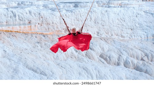 A young woman with blond hair is swaying on swing over Natural travertine pools and terraces in Pamukkale. Cotton castle in southwestern Turkey - Powered by Shutterstock