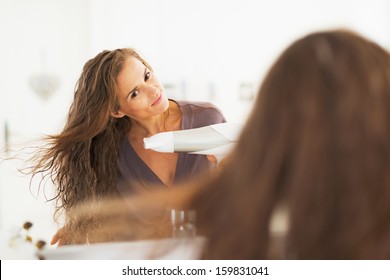 Young Woman Blow Drying Hair In Bathroom