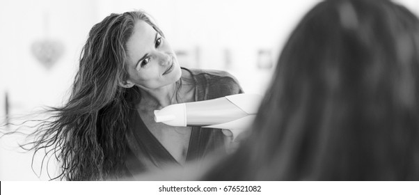 Young Woman Blow Drying Hair In Bathroom