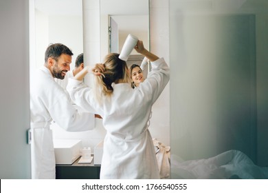 Young woman blow-drying hair with boyfriend standing next to her in bathroom