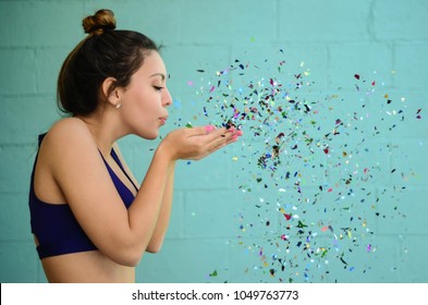 young woman blowing glitter in sports bra on blue background