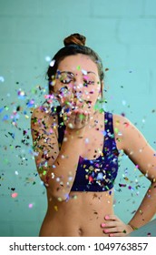 Young Woman Blowing Glitter In Sports Bra On Blue Background