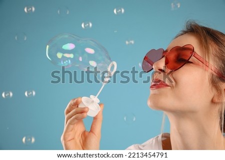 Young woman blowing soap bubbles on light blue background, closeup. Space for text
