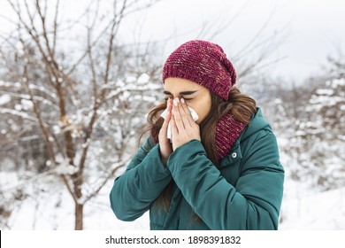 Young Woman Blowing In A Tissue In A Cold Winter With A Snowy Mountain In The Background. Portrait Of A Woman With Tissue In Hands Looking Away. Girl Has The Flu And Running Nose