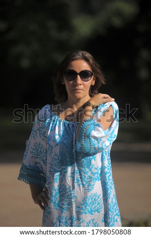 young woman in a blue dress and sunglasses in the summer in the park