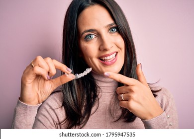 Young Woman With Blue Eyes Holding Clear Aligner Standing Over Pink Background Very Happy Pointing With Hand And Finger