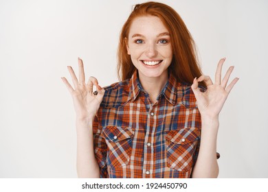 Young woman with blue eyes and red hair saying yes, showing okay sign and nod in approval, smiling satisfied with good choice, white background. - Shutterstock ID 1924450790