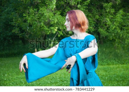 Young woman in blue fantasy dress dancing in the forest