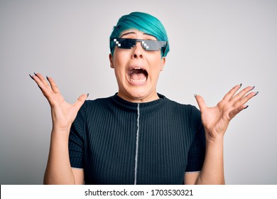 Young woman with blue fashion hair wearing thug life sunglasses over white background celebrating mad and crazy for success with arms raised and closed eyes screaming excited. Winner concept