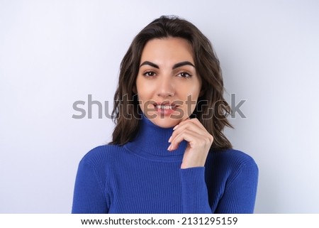 Young woman in a blue golf turtleneck on a white background looking at the camera with a confident smile
