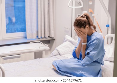 young woman in a blue hospital gown sits alone on a bed in a private room in a clinic, expressing her concern about the results of an examination, covering her face with both palms, - Powered by Shutterstock