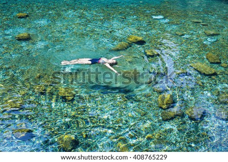 Young woman in blue swimsuit swimming and relaxing in the blue water sea. Top view, general plan with copy space.