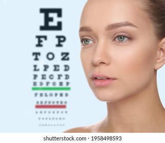 Young Woman And Blurred Eye Chart On Background. Visiting Ophthalmologist 