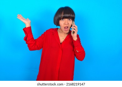 Young Woman With Bob Haircut Wearing Red Shirt Over Blue Wall Talking On The Phone Stressed With Hand On Face, Shocked With Shame And Surprise Face, Angry And Frustrated. Fear And Upset For Mistake.