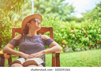 Young Woman With Book Sitting On Chair In Green Garden Terrace