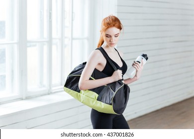 Young Woman With Bottle Of Water And Sports Bag In The Gym