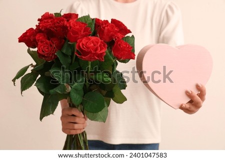 Young woman with bouquet of beautiful red roses and gift box on white background. Valentine's day celebration