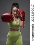 Young woman boxer in red boxing gloves, punching, isolated on gray background