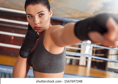 Young woman boxer wearing bandage tape around hands exercise hit standing near boxing ring motivated close-up - Powered by Shutterstock