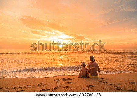 Young woman and boy, mother and son sitting on the beach at sunset, Kalutara, Sri Lanka