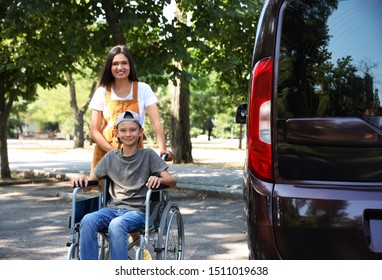 Young Woman With Boy In Wheelchair Near Van Outdoors