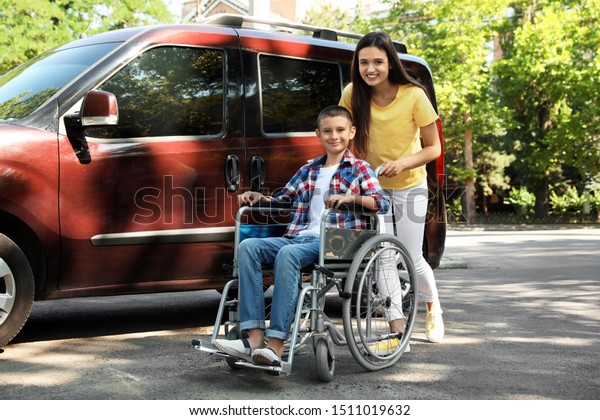 Young\
woman with boy in wheelchair near van\
outdoors