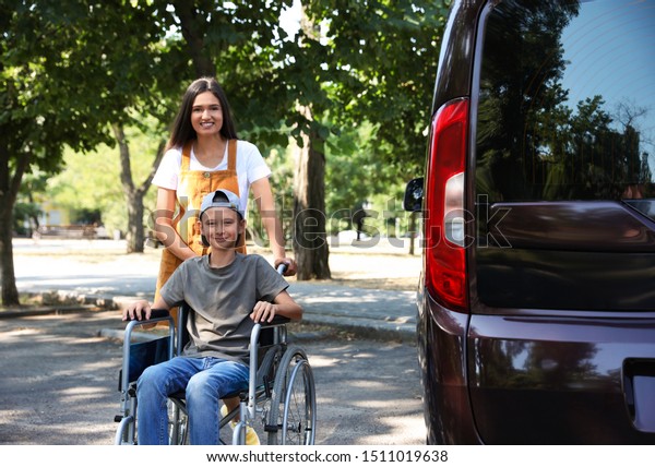 Young\
woman with boy in wheelchair near van\
outdoors