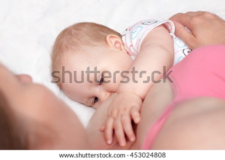 A young woman breast-feeding a baby lying on the bed