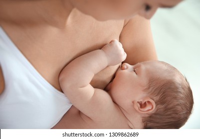 Young woman breastfeeding her baby on light background, closeup