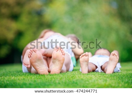 Young woman breastfeeding toddler son, eldest son relaxing on grass beside mother, shallow depth of field