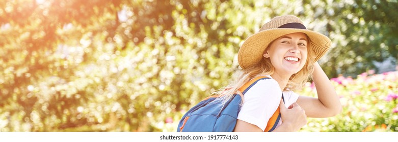 Young Woman With Bright Backpack. Local Tourist. Summer Sunny Day. Green Background. Staycation Weekend. Female Person In Hat And White T-shirt. Smiling Outdoors Portrait