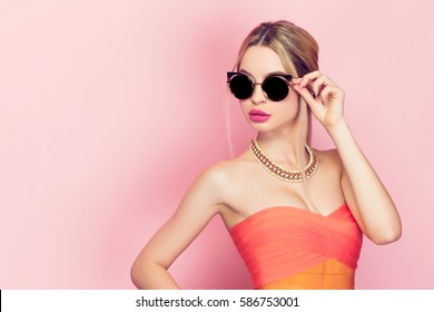 Young Woman In Bright Dress Touching The Sunglasses On The Pink Background.