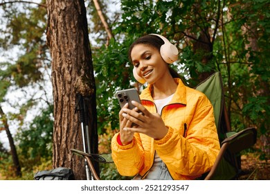 A young woman in a bright jacket relaxes in the forest, enjoying the beauty of autumn while using her phone. - Powered by Shutterstock