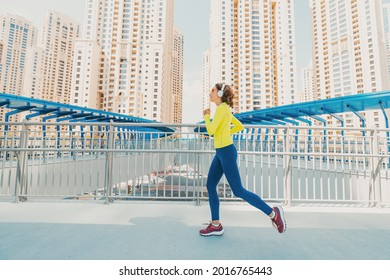 Young woman in bright sportswear quickly runs across a pedestrian bridge in the Dubai Marina district. The concept of a female healthy lifestyle and fitness - Powered by Shutterstock