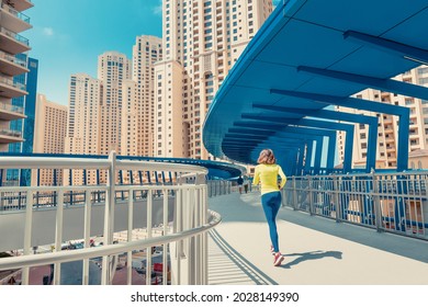 Young woman in bright sportswear quickly runs across a pedestrian bridge in the Dubai Marina district. The concept of a female healthy lifestyle and fitness - Powered by Shutterstock