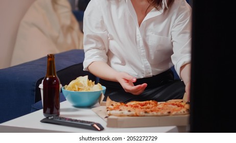 Young Woman Bringing Pizza In Living Room On Table To Eat While Watching Television After Work. Hungry Person With Snacks, Fast Food Meal And Bottle Of Beer Enjoying Takeaway Food At Home