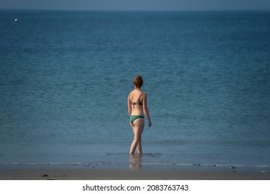 Young Woman With Brown Hair Stands In The Sea. She Looks Over Her Shoulder At Something White In The Blue Water. Alone In The World, Vacation, Freedom