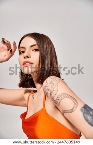 A young woman with brunette hair poses confidently in orange top.