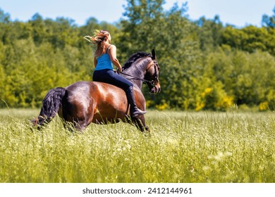 Young woman with brunette long hair rides bareback with her brown horse across a summer meadow, dressed in a blue tank top and riding pants with boots. - Powered by Shutterstock