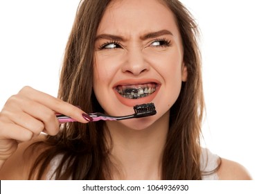 Young Woman Brushing Her Teeth With A Black Tooth Paste With Active Charcoal, And Black Tooth Brush On White Background