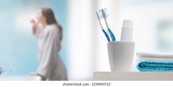 Young woman brushing teeth in the bathroom, toothbrushes and toothpaste in the foreground - Powered by Shutterstock