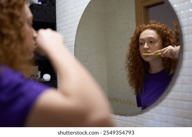 Young woman brushing teeth in bathroom mirror reflection - Powered by Shutterstock