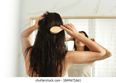 Young Woman Brushing Wet Hair Near Mirror At Home, Back View