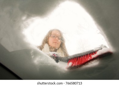 A Young Woman Brusing Snow Off Her Windsheild Looking From Inside The Car