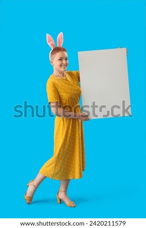 Young woman with bunny ears and blank poster on blue background. Easter celebration