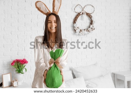 Young woman with bunny ears and Easter gift egg in bedroom