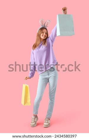 Young woman in bunny ears with shopping bags on pink background. Easter celebration