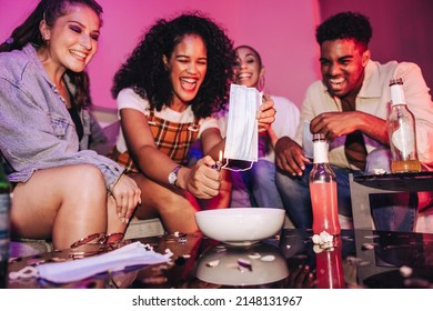 Young Woman Burning A Face Mask At A Post-pandemic House Party. Group Of Happy Young People Celebrating The End Of The Covid-19 Pandemic. Friends Enjoying Their First Post-quarantine Weekend.