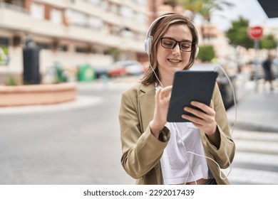 Young woman business worker using touchpad and headphones at street - Powered by Shutterstock