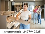 Young woman buyer chooses sample of laminate flooring in hardware store